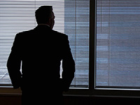 silhouette of business man staring out highrise window through blinds